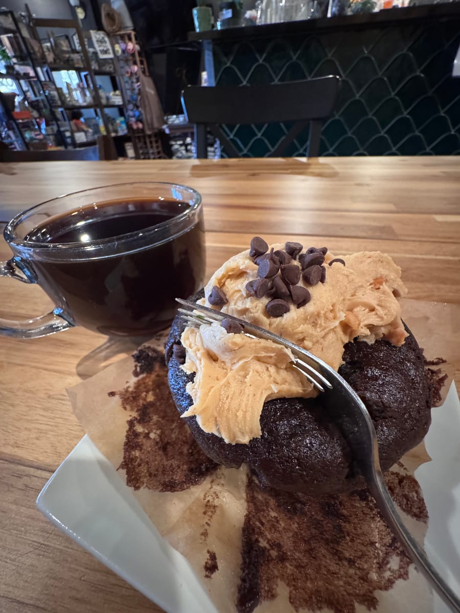 A chocolate muffin with peanut butter frosting and chocolate chips beside a glass mug of coffee